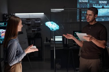 Üç boyutlu sanal araba modelini gösteren tabletli kendinden emin genç erkek mühendis, olasılıklarını bayan meslektaşına açıklarken...