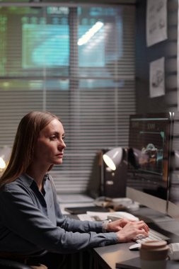 Gri gömlekli genç ciddi kadın tasarımcı ofisteki masaüstü bilgisayarının önünde oturuyor ve yeni grafik araba modeli yaratıyor.