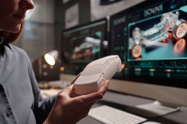 Genç bayan mühendisin elindeki beyaz plastik araba modeli veya iş yerinde bilgisayarlı otomobil tasarımcısı.