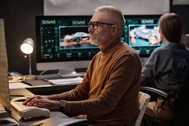 Ciddi yetişkin erkek mühendis bilgisayar ekranına bakıyor ve yaratıcı proje üzerinde çalışırken klavyenin tuşlarına basıyor