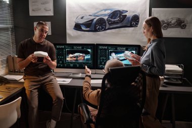 Olgun erkek patron bilgisayarların önünde koltukta oturuyor ve astlarıyla iletişim kurarken ekrandaki araba modelini gösteriyor.