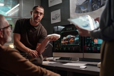 Elinde araba modeliyle genç ve ciddi bir erkek tasarımcı sunum sırasında tabletli iş kadınına bakıyor.