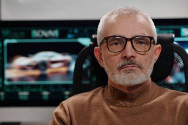 Ciddi bir yetişkin erkek otomobil tasarımcısının yüzü bilgisayar ekranı karşısında kameraya gözlüklerle bakıyor.