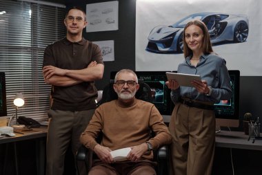 Ofiste veya büroda yeni bir proje üzerinde çalışırken kameraya bakan kendinden emin üç otomobil tasarımcısı grubu