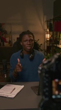 Ev kayıt stüdyosunda kameranın önünde oturmuş canlı yayında çete şiddeti hakkında konuşurken el kol hareketi yapan endişeli Afrikalı Amerikalı erkek podcaster.