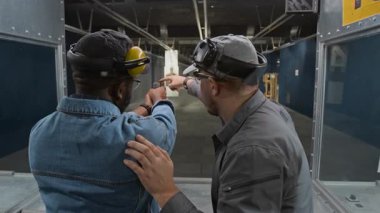 Kafkas erkek atış koçunun orta sahası. Kapalı alandaki Afrikalı Amerikalı erkek müşterilere silah atışı tekniği öğretiyor. Silah namlusundaki hedef ve silah menziline işaret ediyor.