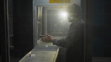 Kamyon şoförü şapkası ve kulaklık takan sivil adam yarı otomatik tabancaya şarjör takıyor, nişan alıyor, hedefe ateş ediyor, kablolar tezgahın üzerine düşüyor.