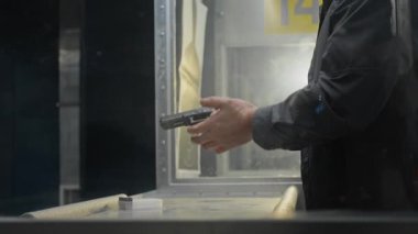 Beyzbol şapkalı adamın yüzünün ve ellerinin arkadan aydınlatılması, kulaklıkların şarjörleri yarı otomatik silaha doldurulması, rafa kaldırılması, hedefe ateşli silah doğrultulması ve galeride pratik yaparken ateş edilmesi.