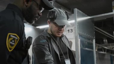 Afrika kökenli Amerikalı kolluk kuvvetleri subayı ve Kafkas erkek atış koçu atış poligonlarında durup çeşitli ateşli silahları tartışırken eğitim için silah seçiyorlar.