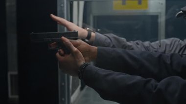 Kafkasyalı erkek koçun, siyahi polis memuruna silah tutmasını ve nişan almasını öğretirken, kapalı alanda atış talimi yaparken, orta boy yakın çekimi.