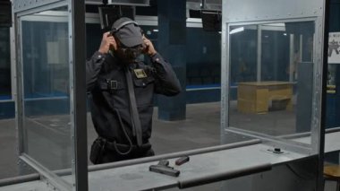 Orta ölçekli, kendinden emin genç Afro-Amerikan polis memurunun atış poligonu önünde durup kulaklıklarını taktıktan sonra tek başına nişancılığı geliştirmek için silah doğrulttuğu bir fotoğraf.