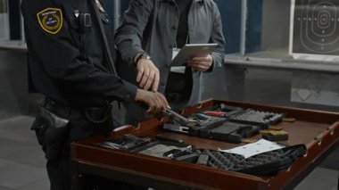 Siyah üniformalı genç siyahi erkek polis memurunun ya da güvenlik görevlisinin orta eğik pozisyonu. Atış poligonunda koçla silah kullanmayı öğrenmeleri, doldurmaları, silah doldurmaları ve soru sormaları.