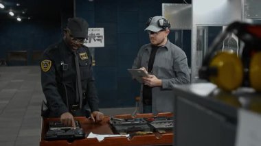 Orta boy üniformalı, rozetli, kılıflı ve tabletli Kafkas atış poligonu sahibi, çeşitli silahların faydalarını tartışan, pratik için silah seçen siyahi erkek polislerle dolu.