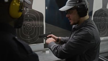 Orta ölçekli beyaz erkek eğitmenin yarı otomatik silah üzerindeki geri tepme etkisini ve kendini yükleme mekanizmasını dinleyen ve kafa sallayan Afrikalı Amerikalı polis akademisine verdiği görüntü.