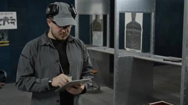 Tabletle çalışan, rezervasyon çizelgesini kontrol eden bir sürü atış poligonu eğitmeni varken, siyah üniformalı polis onları oyalamak için yürüyor, kulaklıklarını takıyor ve hedefe nişan alıyor.