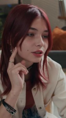 Şık giyinmiş, burnuna piercing takılmış, bacak bacak üstüne atmış, modern ofisteki psikologla pozitif konuşan güzel, kızıl saçlı, beyaz bir kızın dikey görüntüsü.