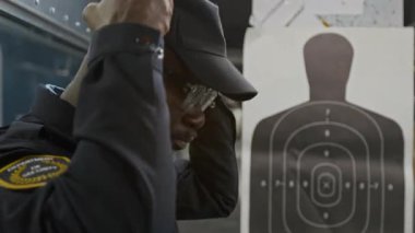 Siyah üniformalı, beysbol şapkalı ve gözlüklü yakışıklı Afro-Amerikan polis memurunun atış taliminden önce koruyucu kulaklık takması.