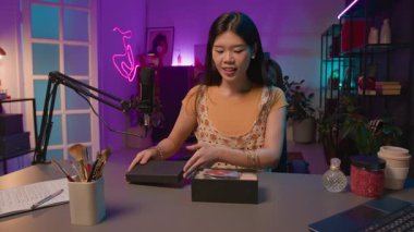 Canlı yayında mor neon kayıt stüdyosunda mikrofonun önünde oturan neşeli Asyalı kadın güzellik etkisinin orta boy UGC görüntüsü.