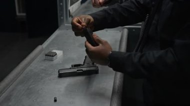 Şarjöre mermi doldurma pratiği yapan Afro-Amerikan polis memurunun orta derecede ellerini ve yüzünü eğip sonra da eğitmenlerin rehberliğinde tabancaya yerleştirip nişan alıyor.