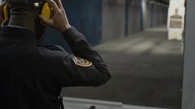 Afrika kökenli Amerikalı kanun adamı koruyucu kulaklıklar takıyor. Atış sahasına, tabancaya ve hedefe nişan alıyor. Atış menzilinde nişancılık becerileri geliştiriyor.