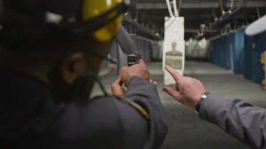 Menzilde atış talimi yapan erkek polis ya da güvenlik görevlisi orta omuzlu, gövde hedefine uzaktan nişan alan ve nişan alan eğitmen eli...