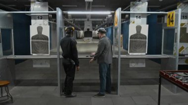 Atış poligonu eğitmeninin hedef belirlemek, polise doğru duruşu göstermek, ilk eğitim oturumunda hataları düzeltmek için hedef alma sistemindeki düğmeye basarak tam yakınlaştırma görüntüsü