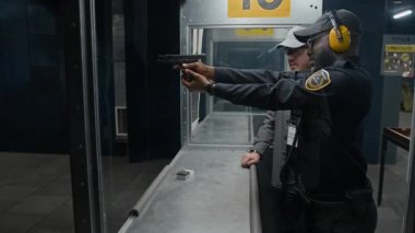 Üniformalı genç siyahi bir polisin poligonda ateş etmeyi öğrenirken, tetiği çekerken, mermi kovanı düşerken, Kafkas eğitmeni onu izlerken ve kavrama konusunda tavsiye verirken orta ölçekli bir fotoğraf.