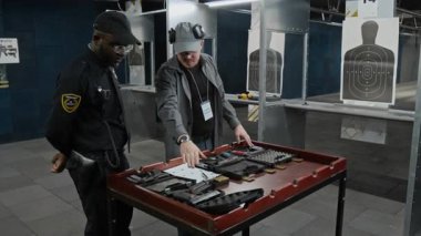 Orta yaşlı, Kafkas erkek eğitmenlerle dolu. Atış taliminden önce siyah üniformalı Afrikalı Amerikalı stajyer polislere atış poligonunda uygun silahları gösteriyor.