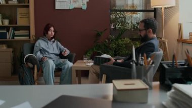 Erkek sakallı bir psikolog, genç beyaz bir kıza terapi seansında aile veya okul baskısıyla ilgili duygusal sorunlar hakkında kağıt havlu sunuyor.