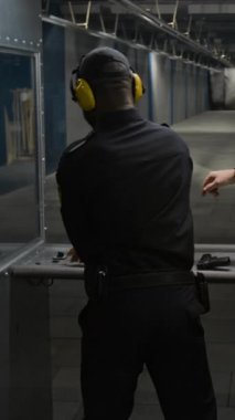 Siyah polis memurunun ve Kafkas erkek eğitmenin dikey arka tarafındaki siluet hedefini kurşun izleriyle birlikte ele geçirip atış ve ıskalamaları atış mesafesinde inceler ve analiz ederler.