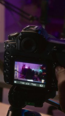 Tripodla profesyonel kamerayı açan, neon ışıklı masaya odaklanan, odak ayarlarını ayarlayan, canlı yayına hazırlanan, tanınamayan genç adamın el dikey yakın çekimi