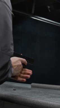 Mermi şarjörünü tabancaya dolduran koruyucu kulaklıklı genç bir adamın dikey yakın çekimi, hedef alma, nişan alma, hedef alma ve sonuçları kontrol etme