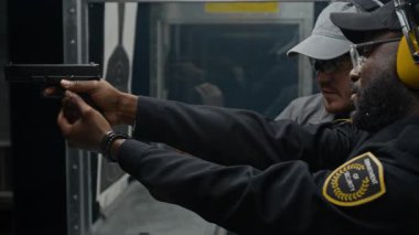 Beyaz tenli genç bir adamın orta ölçekli bir yakın çekimi. Siyahi polis memuruna silah kullanma konusunda talimat veriyor. Hedefe ateş etme emri veriyor ve geri bildirim veriyor.