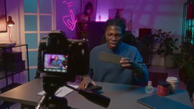 Üç ayaklı kameranın orta boy görüntüsü. Neşeli Afrikalı Amerikalı erkek etkili kutu açıyor. Markalı kozmetikler canlı yayında ve abonelere göz bantları tanıtılıyor.
