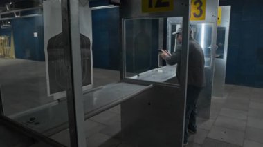 Tam kavisli, odaklanmış, koruyucu kulaklık takan, kapalı alanda duran, yarı otomatik tabancayı ateşleyen, nişan alan, ateş eden, hedef alan, hedef kontrolü yapan beyaz bir adam.