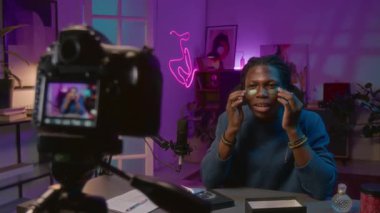 Canlı yayın sırasında göz bantlarını gençleştirmeye çalışan mutlu, kendinden emin Afrikalı Amerikalı erkek blog yazarı, güzellik prosedürleri hakkında abonelerle konuşurken ve el kol hareketi yaparken.