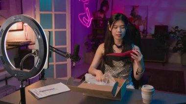 Canlı yayında Neon Stüdyoları 'nda masa başında çalışan, üzerinde şık kırmızı süet topuklu ayakkabılar olan kutuları açan, işçiliğini kontrol eden ve onlara hayran olan neşeli Çinli kadınların orta boy görüntüsü.