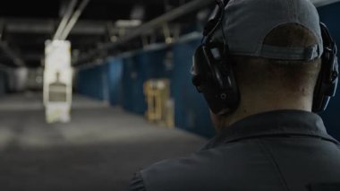 Beyzbol şapkalı, tabancasını kaldıran, uzaktan siluet hedefine nişan alan, ateş eden, atış talimi yapan, tanınmayan bir gencin arka görüntüsü.