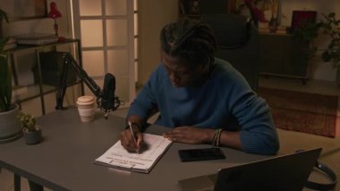 Odaklanmış genç Afro-Amerikan bir adamın podcast programı için içerik planı üzerinde çalışırken popüler sosyal medya eğilimlerini ve laptoptaki haberleri araştırdığı orta boy bir fotoğraf.