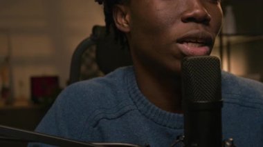 Canlı yayında güncel konuları tartışırken, merkez stüdyoda mikrofona konuşan kimliği belirsiz siyahi erkek podcaster 'ın orta ve alt yüzünün görüntüsü.