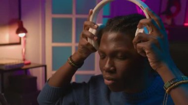 Yeni beyaz kulaklıklar deneyen, gözlerini kapatan, ses kalitesinin keyfini çıkaran ve canlı yayındaki abonelere övgüler yağdıran Afro-Amerikan erkek etkisinin yakın çekimi.