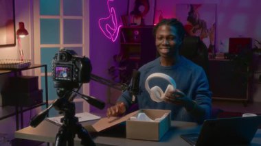 Sosyal medyada ya da online dükkanda canlı yayında yeni beyaz kulaklıklarla kutuları açan Afro-Amerikan erkek blog yazarının orta boy görüntüsü. Tasarıma hayran kaldıktan sonra takıyor.