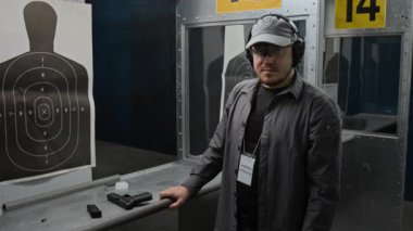 Beyaz erkek atış poligonu koçunun orta boy portresi gövde hedefinin ve yarı otomatik silahın yanında duruyor kameraya bakıyor ve güvenle gülümsüyor.