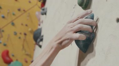 Modern spor kompleksinde duvar tırmanma pratiği yapan erkek sporcuların yakın çekimi. Tebeşir magnezyum tozuyla kaplı erkek eller duvara tırmanıyor.