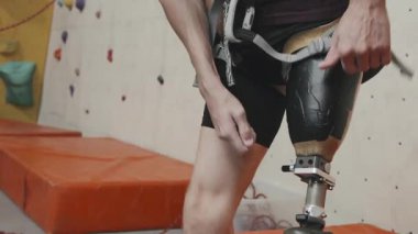 Robotik bacağı olan, duvar tırmanışı için güvenlik ekipmanı takan tanınmamış sporcunun orta kısmı modern kapalı spor merkezinde duruyor. Güç ve motivasyon kavramı.