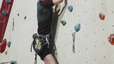 Çağdaş spor merkezinde bacağı kesilmiş güçlü bir sporcunun güvenlik ekipmanlarıyla duvarlara tırmanışının izini sürüyorum.