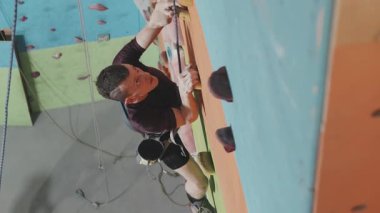 Ampüte olmuş bacağı kopmuş ve güvenlik ekipmanlarıyla duvara tırmanan kararlı atletik adamın yavaş yavaş izini sürüyorum. Modern spor kompleksinin duvarına tırmanıyor.