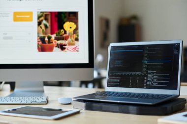 Bilgisayarında kodlar olan dizüstü bilgisayar, programcının iş yerinde, ofisinde resim oluşturucu olan bilgisayara karşı duruyor.