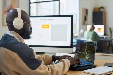 Genç, ciddi bir ofis çalışanı kulaklıkla dizüstü bilgisayarda yazarken görüntü oluşturucu ile verileri deşifre ediyor.