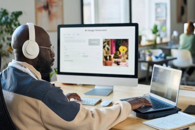 İş sırasında aynı anda iki masaüstü bilgisayarı kullanan kulaklıklı genç iş adamının yan görüntüsü